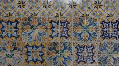 Close view of multicolored ceramic tiles with blue scrolling foliage, geometric compartments, and yellow, green, orange, and white details.