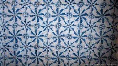 Close view of repeating blue-and-white ceramic tiles with interlocking floral and geometric motifs and areas of surface wear.