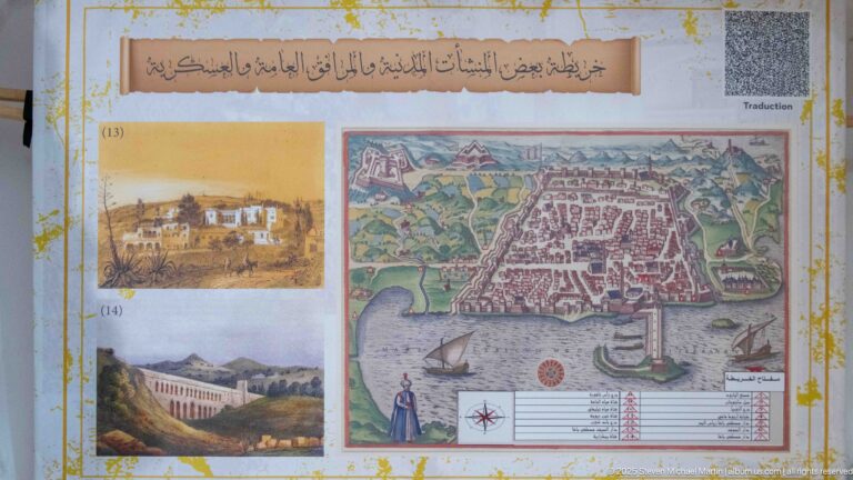 Museum-style panel with Arabic text, small historical views, and a large colored map or plan of coastal Algiers.