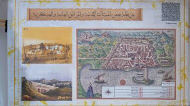 Museum-style panel with Arabic text, small historical views, and a large colored map or plan of coastal Algiers.