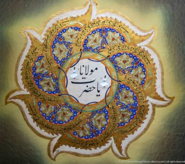 Six-lobed blue-and-gold illuminated medallion with bold Arabic calligraphy in a white central circle.