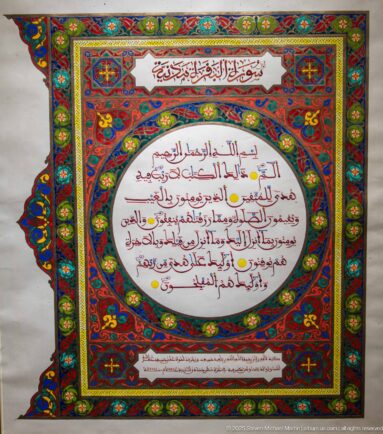 Arabic manuscript-style page with red text in a white oval, surrounded by elaborate red, blue, green, and gold illuminated borders.