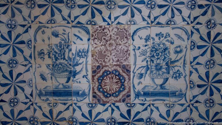 Decorative tiled wall with two blue-and-white flower vases flanking a multicolored central medallion amid geometric blue tiles.
