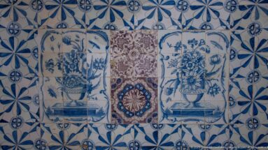 Decorative tiled wall with two blue-and-white flower vases flanking a multicolored central medallion amid geometric blue tiles.