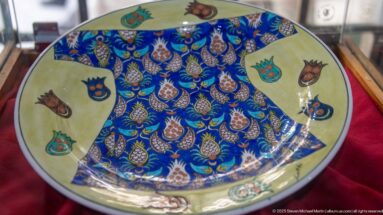 Shallow ceramic dish with cobalt-blue patterned center, repeated multicolored floral buds, and pale rim panels with isolated motifs.