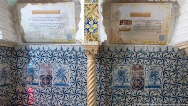 Interior wall covered in blue-and-white tiles, with a spiral stone column and Arabic interpretive panels mounted above.