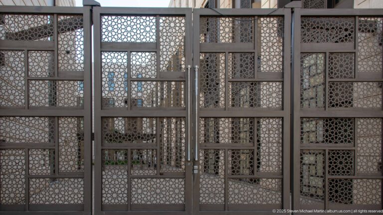 Large rectangular metal screen with central double doors and dense repeating geometric lattice panels.