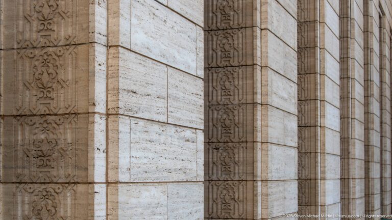 Close view of pale stone wall with narrow vertical carved bands of repeating ornamental motifs.