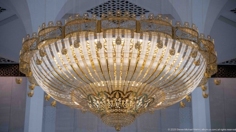 Large gold-toned crystal chandelier with concentric glass bands and hanging drops inside the mosque.