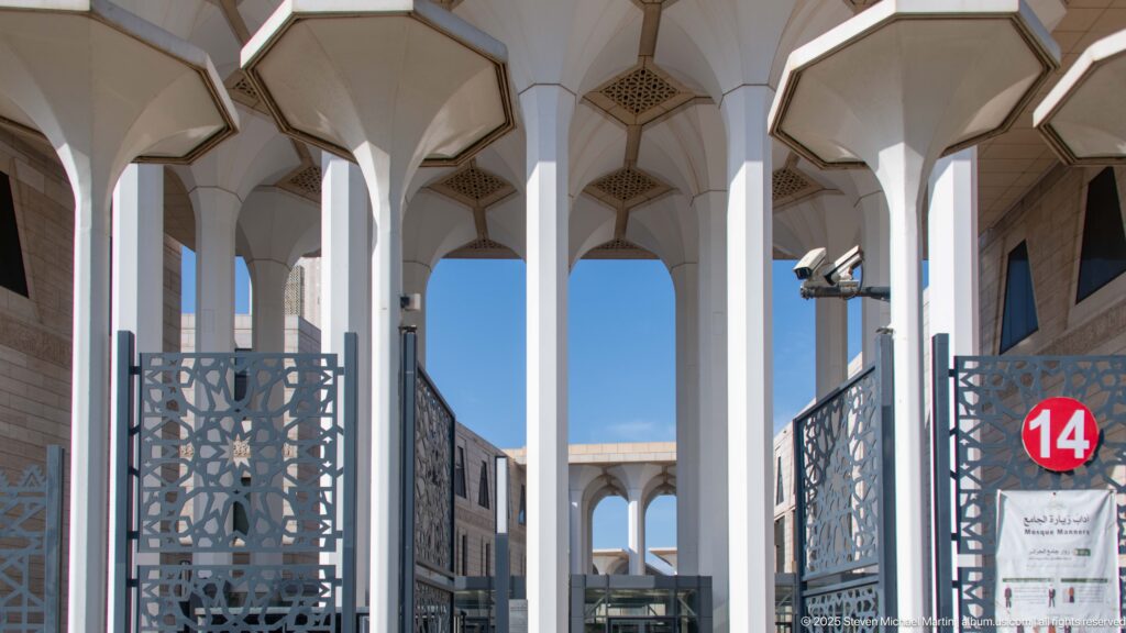 Tall white flared columns and geometric ceiling grilles at an entrance portico of the Great Mosque of Algiers.