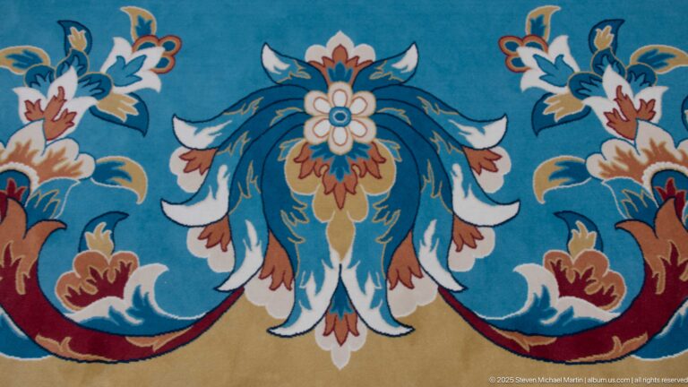Close-up of blue mosque carpet with a symmetrical turquoise, cream, rust, and ochre floral motif.