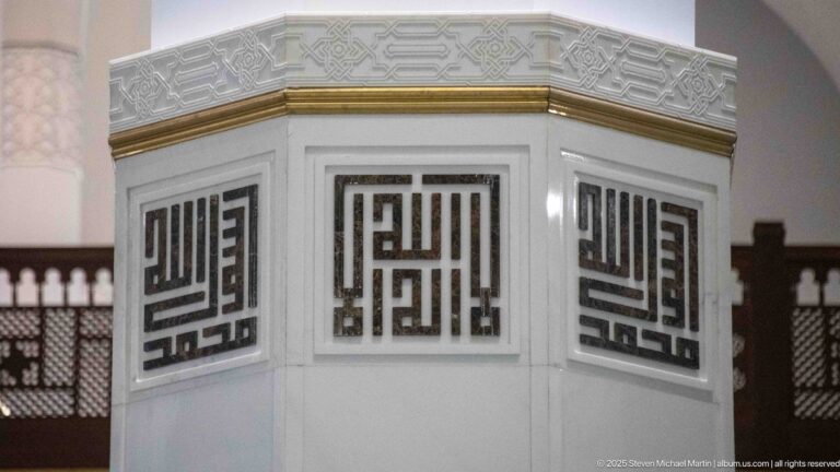 White octagonal structure with dark square geometric calligraphic panels and a narrow gold band.