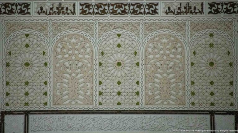 Repeating arched ornamental panels sit above a horizontal Arabic calligraphic band in pale, green, and dark tones.