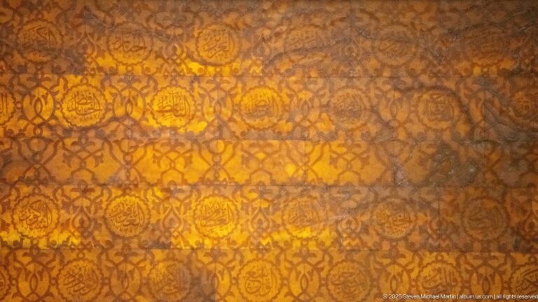 Amber light shines through a dense repeating arabesque pattern of rosettes and scrolling forms.