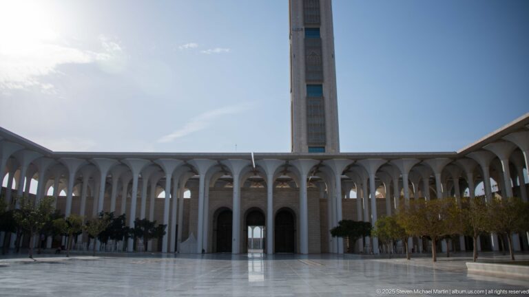 White arcades surround a paved courtyard with trees, while the tall rectangular minaret rises at center.