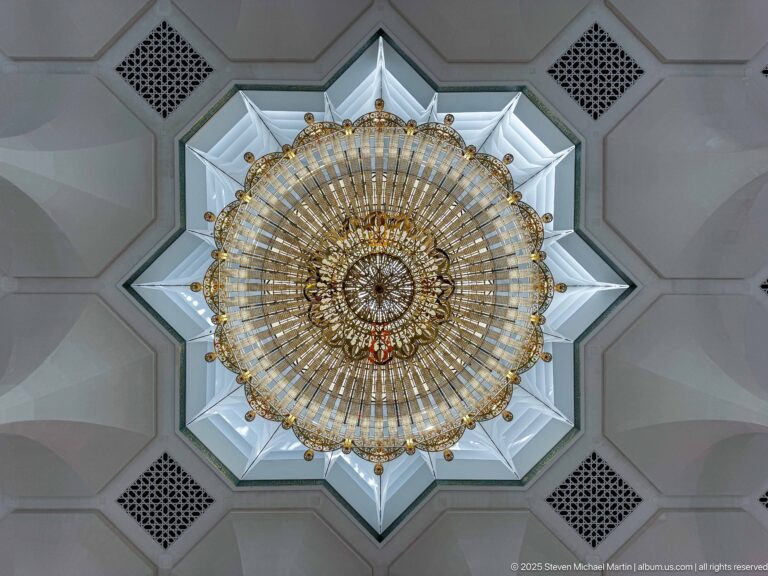 Round gilded chandelier centered in a star-shaped white ceiling recess with dark ventilation grilles.