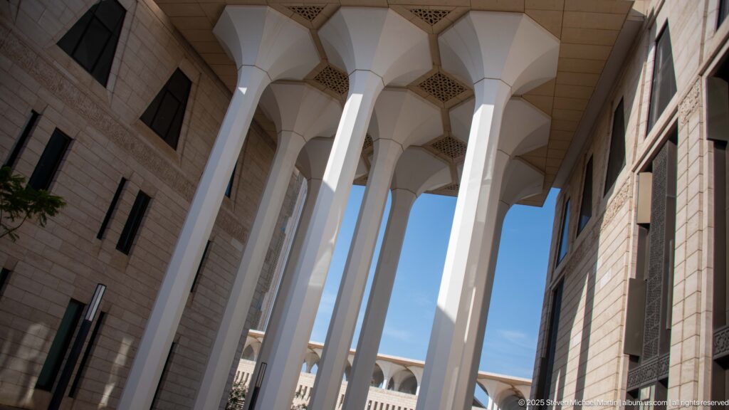 Oblique upward view of tall white flared columns supporting a portico canopy between stone walls.