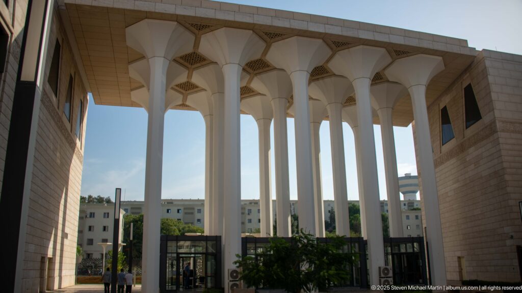 Tall white entrance columns at the mosque framing distant apartment buildings beyond the complex.