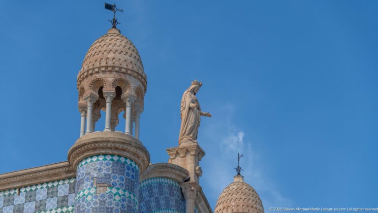 Small domed turret and standing roofline statue above blue patterned tilework at Notre-Dame d’Afrique.