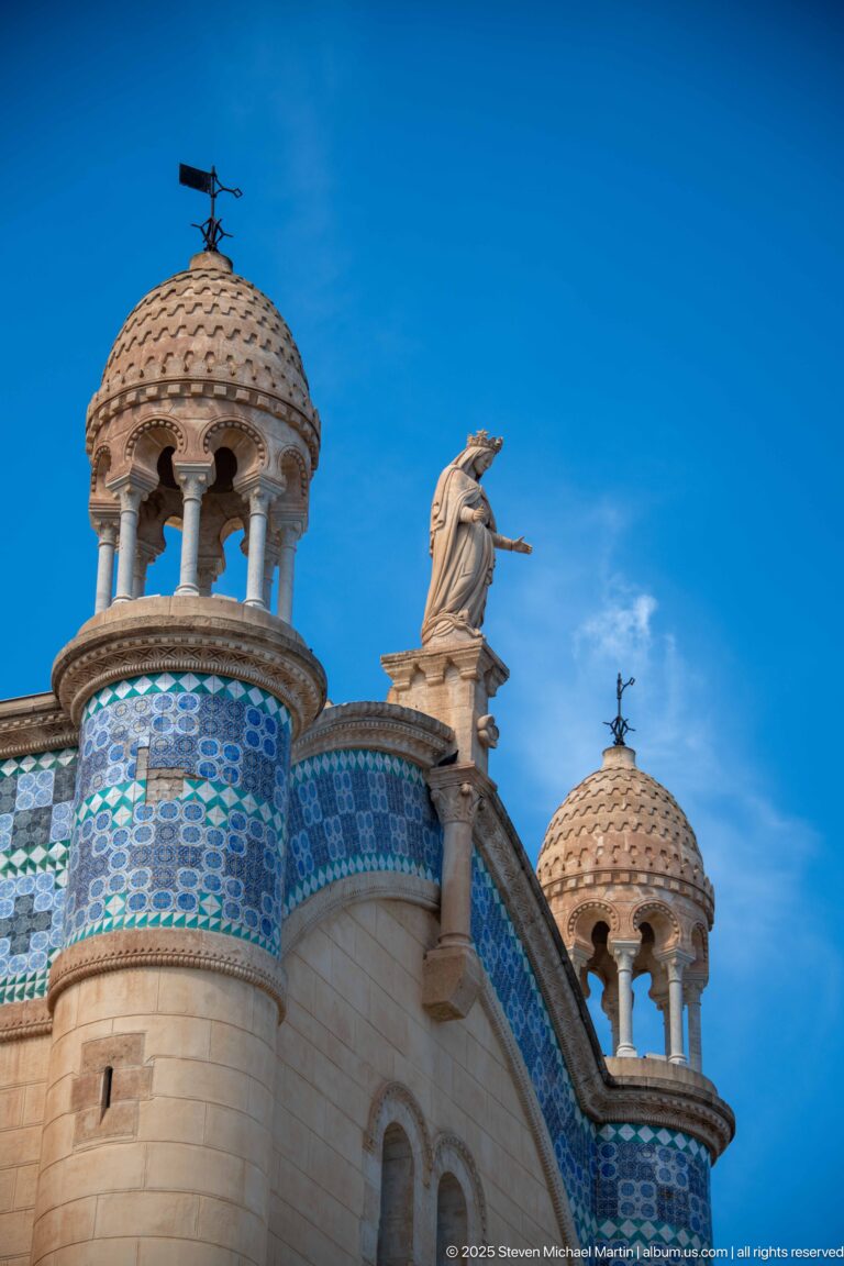Curved roofline of Notre-Dame d’Afrique with blue tile panels, small open turrets, and standing statues.