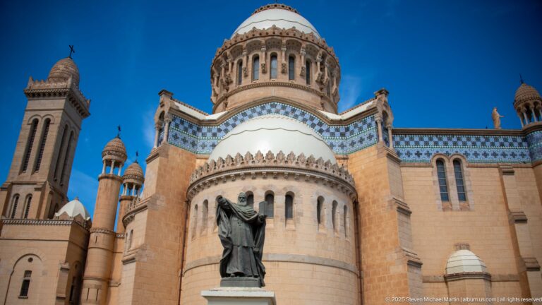 Religious statue in front of the rounded apse and central dome of Notre-Dame d’Afrique.