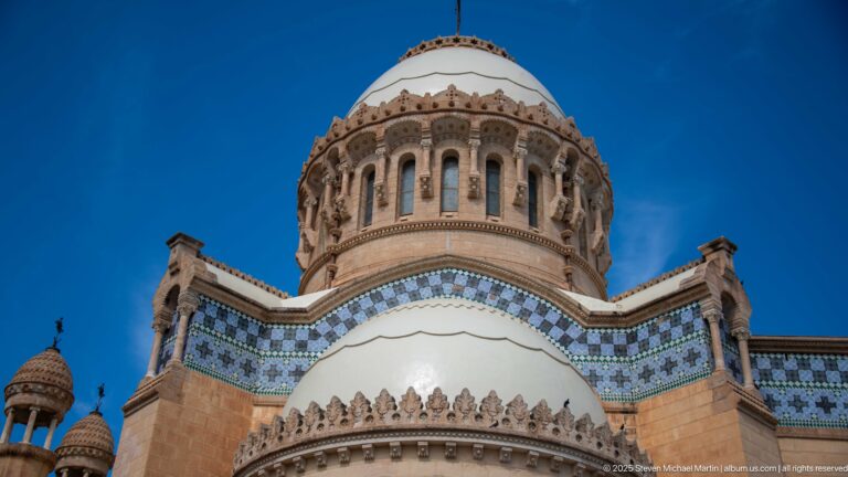 Close-up of Notre-Dame d’Afrique’s central dome drum, arched openings, blue tiled cornice, and scalloped lower dome.