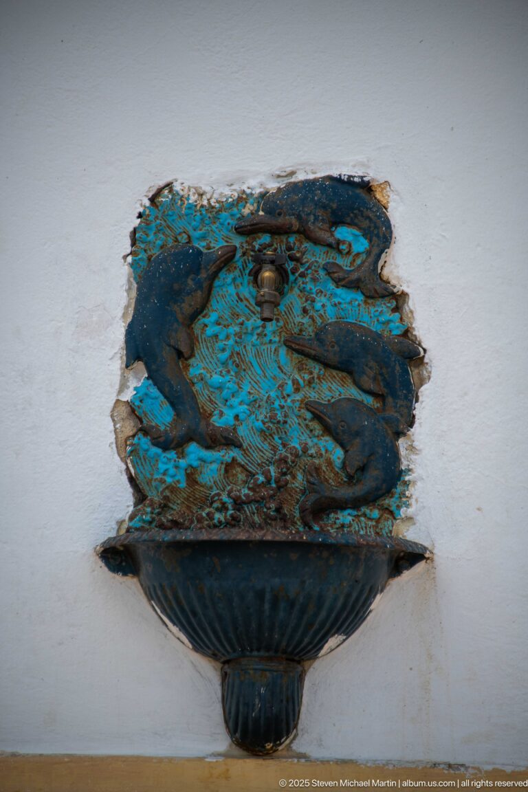 Weathered turquoise wall-mounted decorative basin or bracket with flaking paint and a dark relief motif.