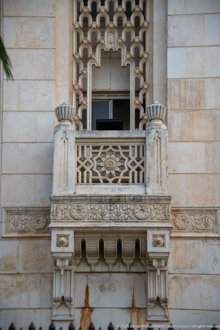 Small carved stone balcony with geometric balustrade and patterned screen on the mosque façade.
