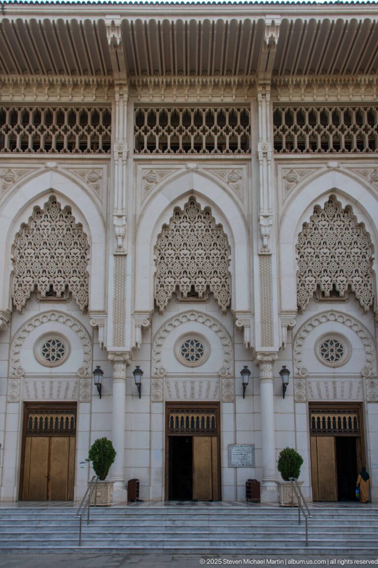 Frontal view of three richly decorated mosque portals beneath a deep roof overhang and screened upper band.