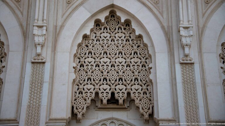 Intricate pale pierced screen with repeating lobed geometric motifs filling a pointed arched façade recess.