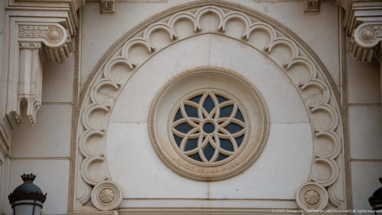 Circular radial rosette window surrounded by concentric carved stone bands on the pale mosque façade.