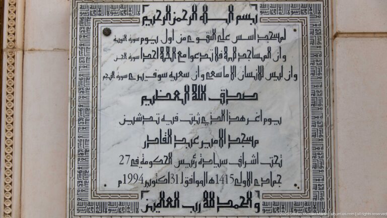 Arabic inscription plaque with decorative border on the mosque wall, including visible dates 1415 and 1994.
