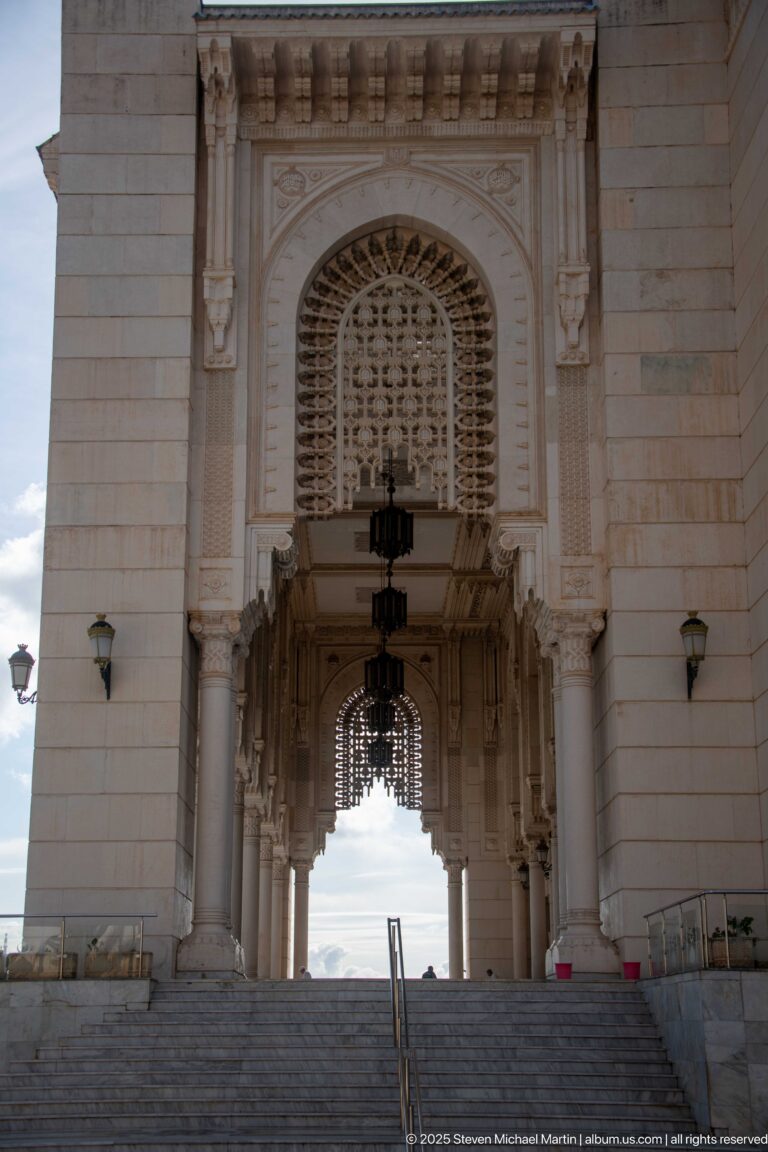 Broad steps leading into a tall columned mosque passage beneath an ornate screened arch.