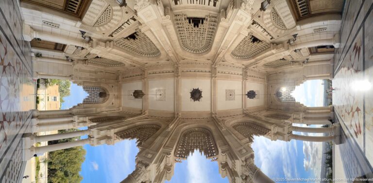 Upward view beneath the mosque portico showing carved vaults, columns, patterned soffits, and openings to blue sky.