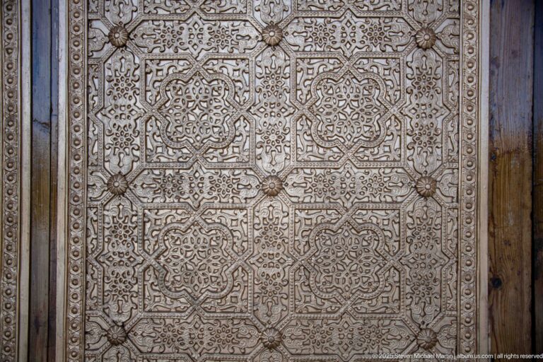 Close detail of a bronze-toned door panel covered with repeating geometric rosettes and intricate raised ornament.