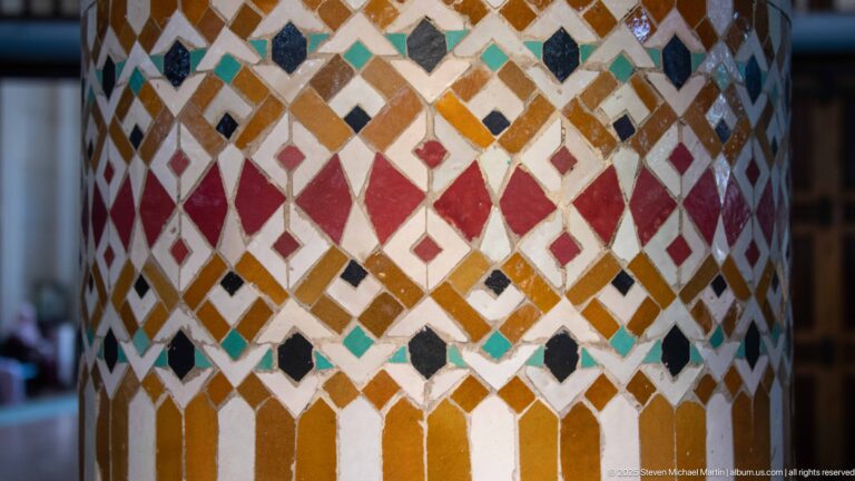 Close detail of a cylindrical column covered in repeating multicolored diamond-pattern mosaic.