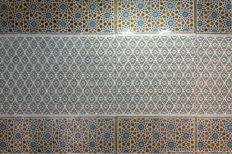 Large wall panel of dense geometric mosaic bordered by multicolored star-pattern bands.
