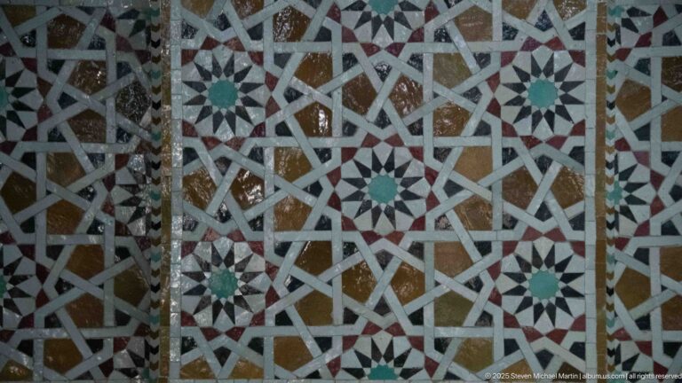 Close-up of interlaced geometric mosaic with white bands, multicolored polygons, and repeated green-centered stars.