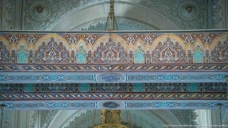 Horizontal bands of turquoise, red, blue, and cream ornament with repeated pointed-arch motifs inside the mosque.