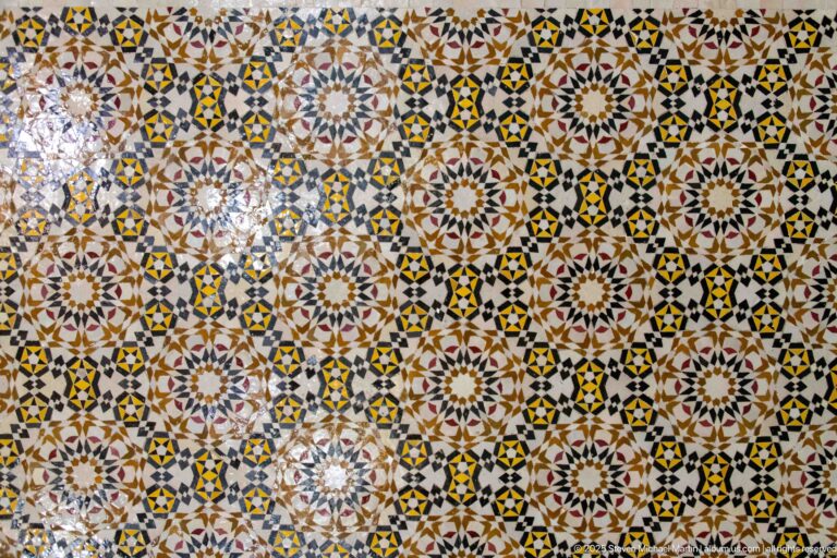 Close view of multicolored geometric tilework formed from repeating stars, rosettes, polygons, and radial motifs.