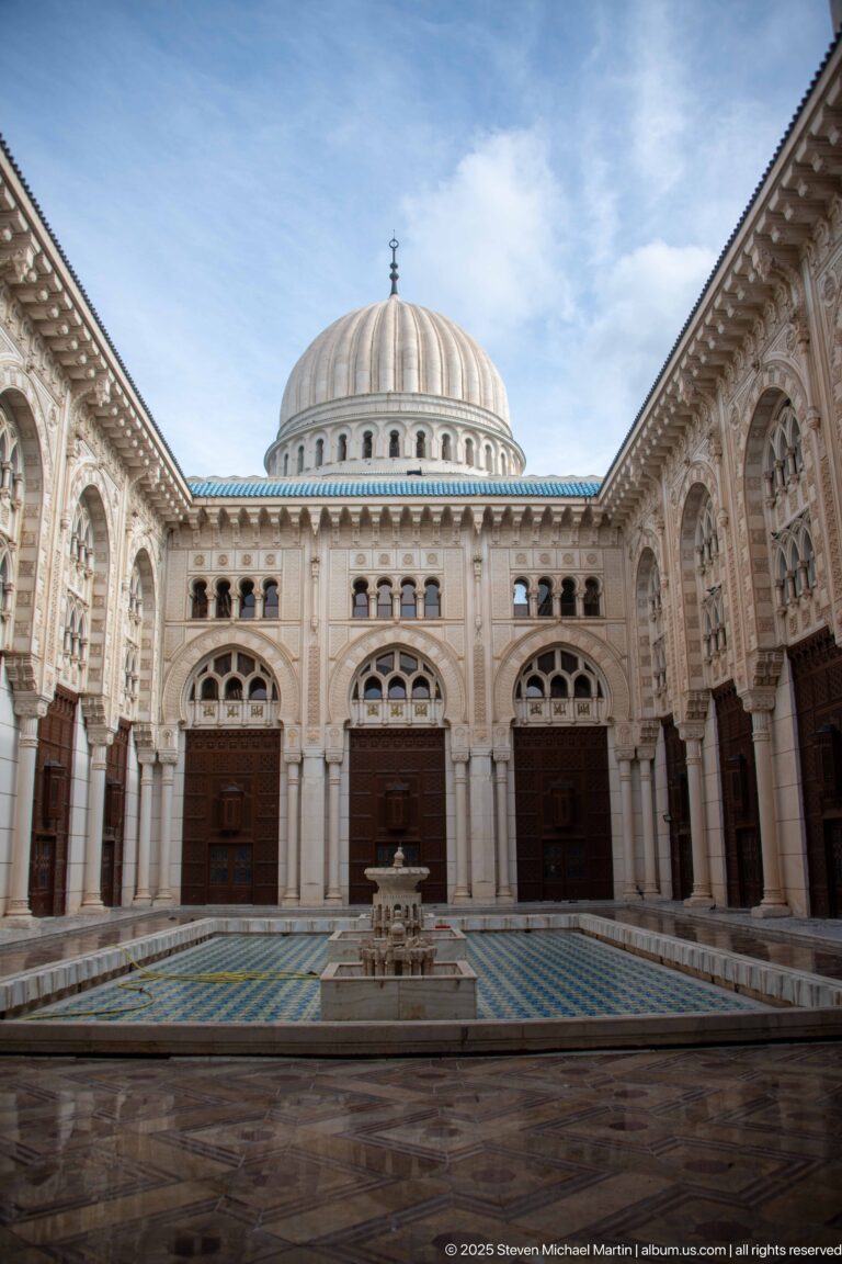Wide symmetrical courtyard view with central fountain, arcaded side walls, three far doorways, and a ribbed dome.