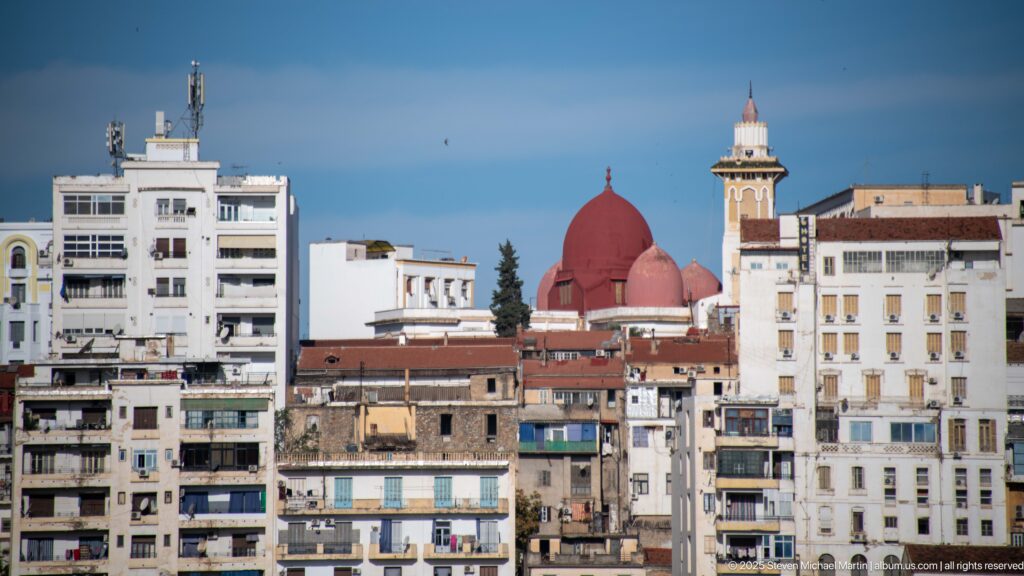 Red-domed religious building and tower rising among dense apartment blocks in central Constantine.