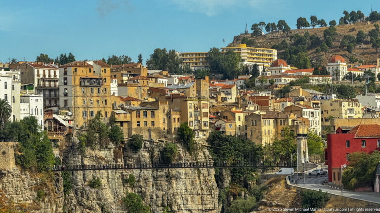 Dense hillside buildings in Constantine rising directly above a rocky gorge, with roads and retaining walls following the cliff edge.