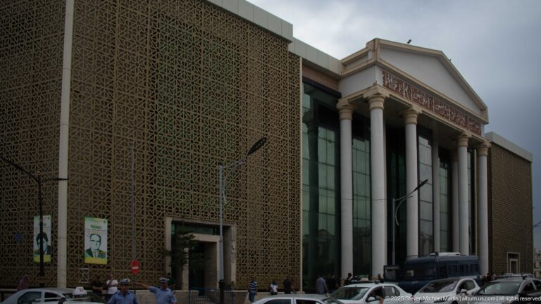Large Constantine building with geometric screen façade, tall columns, triangular pediment, and central glass entrance.