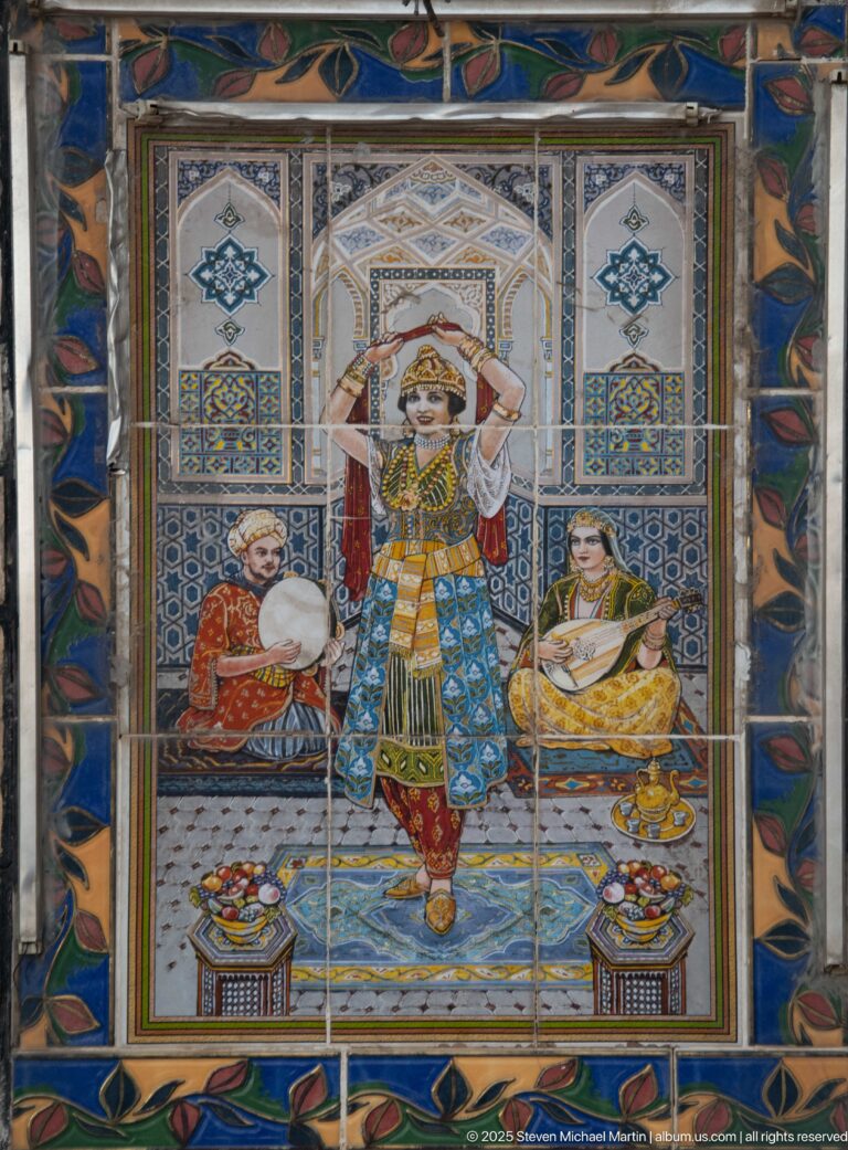 Colorful ceramic tile panel showing a central dancer with seated musicians, patterned costumes, vessels, and blue geometric borders.