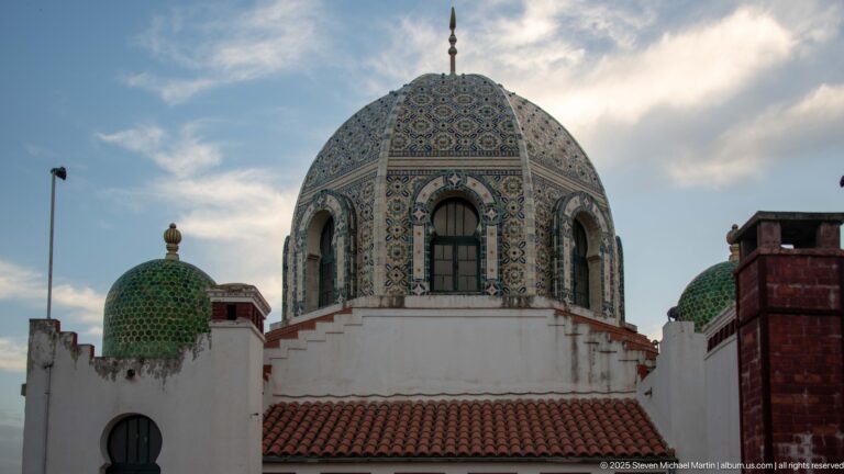 Large blue-and-green patterned tiled dome with arched windows and smaller green domes above white walls.