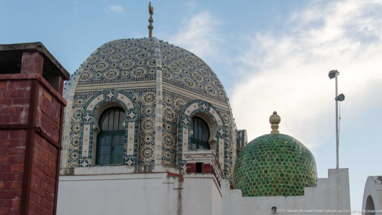 Close oblique view of patterned blue tiled dome with arched windows beside a smaller green dome.