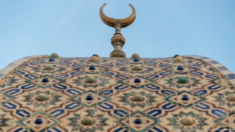 Crescent finial above blue, green, and cream geometric tilework with raised ceramic bosses on a dome.