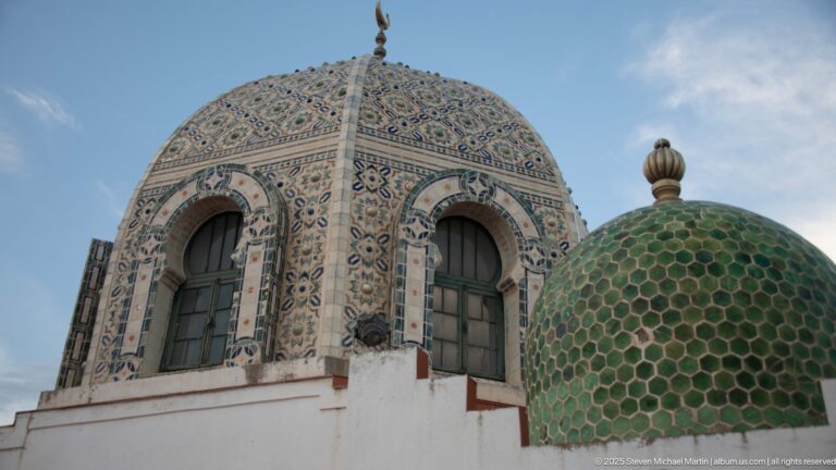 Two ornate domes, one patterned with multicolored tiles and arched windows and one covered in green scale-like tiles.