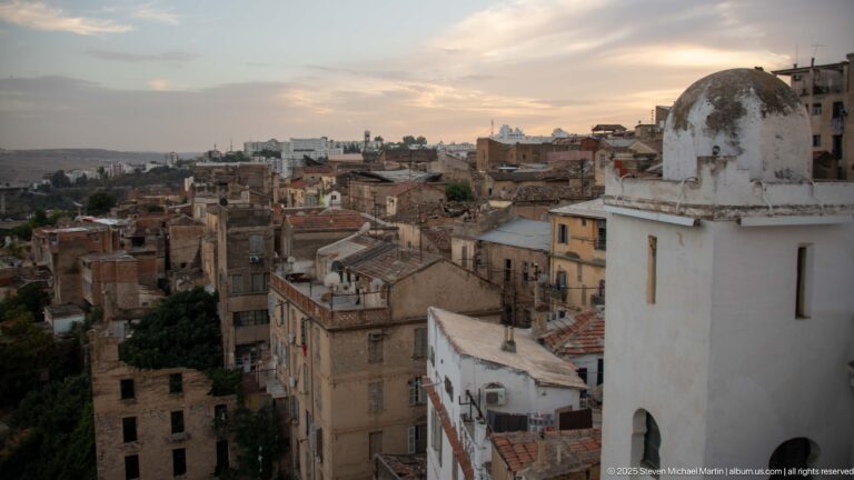 Dense Constantine rooftops at dusk with a small white domed structure in the foreground and closely packed buildings beyond.